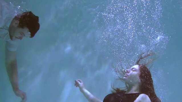 A woman and a guy are swimming underwater. A woman kisses a guy underwater.