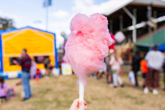 Hand holding pink cotton candy at colourful fair event