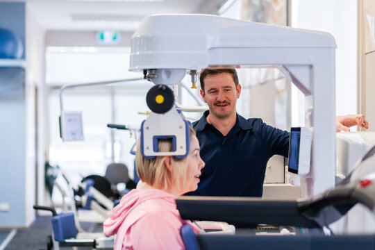 Happy physio standing beside woman using physical therapy equipment