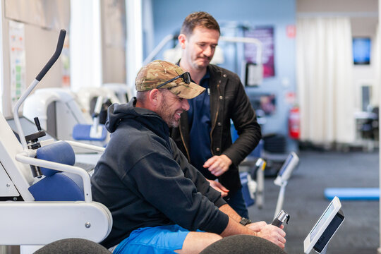 happy smiling male physio client with physiotherapist using exercise therapy equipment