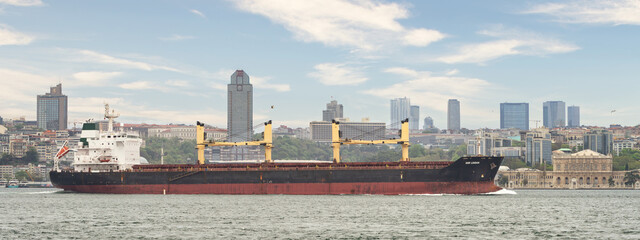 DSM London, large cargo ship sails through the Bosphorus Strait, a narrow waterway that connects the Black Sea to the Sea of Marmara. The ship is dwarfed by the towering buildings of Istanbul, Turkey