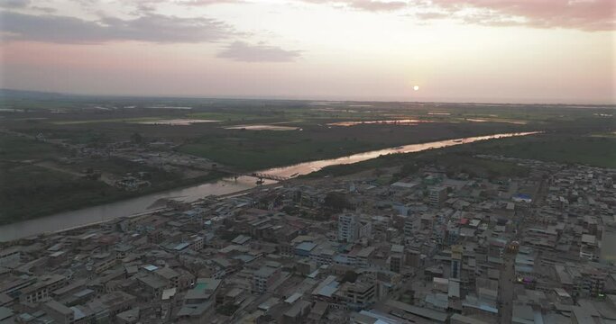 Aerial shot of Tumbes river, bridge and city at sunset. Tropical city at north of Per&uacute;. 