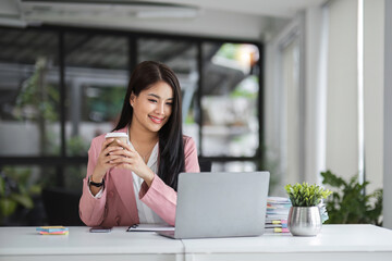 Businesswoman working with laptop computer while having a leisurely cup of coffee at the office in the morning.