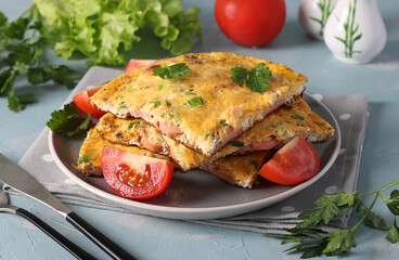 Omelet with sausages, cheese and parsley served with tomatoes on a gray plate on a light blue background.