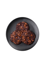 Delicious fresh oatmeal round cookies with chocolate on a black ceramic plate