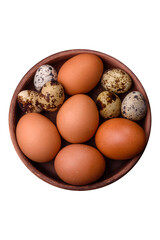 Raw chicken and quail eggs in a brown ceramic bowl on a dark concrete background
