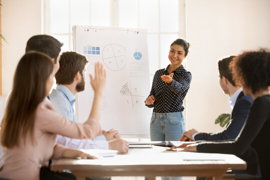 Smiling young indian female presenter or coach interact with motivated employee raise hand at briefing, happy ethnic woman trainer talk answer question of worker at business meeting or training - Powered by Adobe