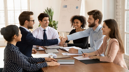 Smiling male business partners handshake close deal make agreement at team meeting in office, happy young businessmen shake hands get acquainted greeting at briefing, partnership concept