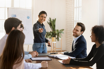Obraz premium Smiling female indian team leader interact with employee at group briefing in office, happy excited diverse multiracial colleagues participate in teambuilding activity at meeting or training together