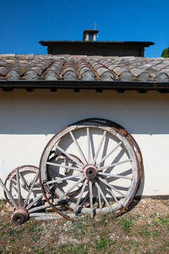 Ancient wooden wheels of a cart leaning against the wall of a rural house, blue sky in the background.