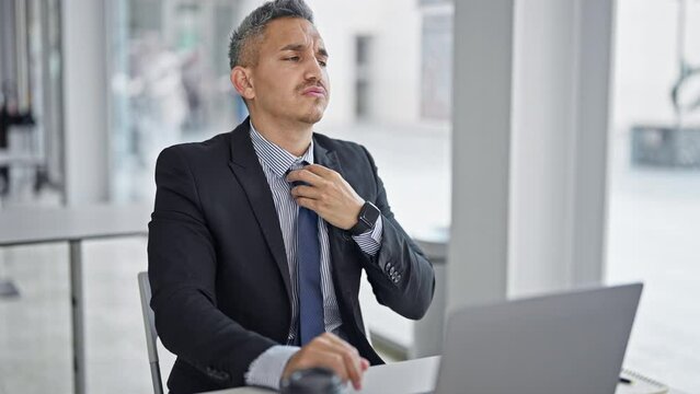 Young hispanic man business worker loosen the tie working at office