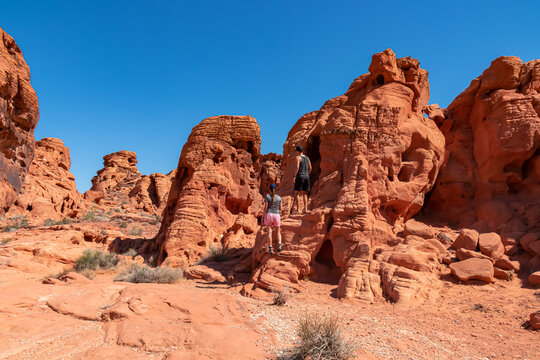 Couple at the entrance of windstone arch (fire cave) in Valley of Fire State Park, Mojave desert, Nevada, USA. Scenic view of beehive shaped red sandstone rock formations. Barren deserted landscape
