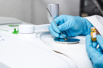 Hand of scientist using a stainless spatula to scoop sample solid from vial to the Fourier...