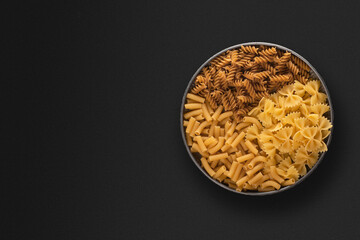 Variety of types and shapes of dry pasta in bowl, top view with copy space for text.