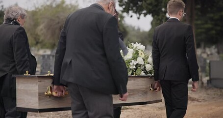 Coffin, men and pallbearers walking at graveyard ceremony outdoor at burial tomb. Death, grief and group casket at cemetery, carrying to funeral and family service of people mourning at windy event
