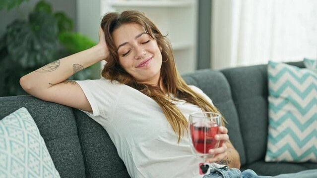 Young beautiful hispanic woman drinking tea relaxed on sofa at home