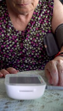 An older woman checks her blood pressure with an electronic blood pressure monitor at home.