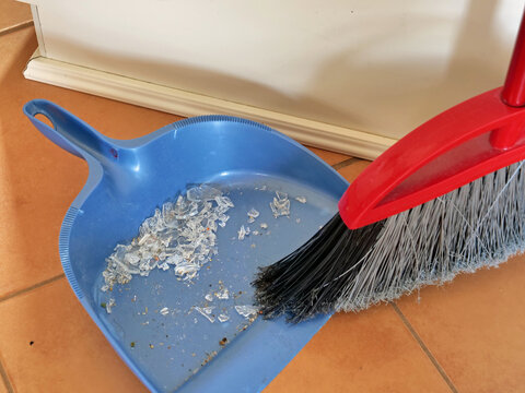 Sweeping shattered glass with sharp edges into the pan with a broom - Powered by Adobe