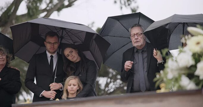 Death, funeral and umbrella, people at coffin for service in graveyard in respect, mourning and support. Flowers, rain and loss, family at casket in cemetery with memory, grief and grave for burial.