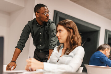Young, multiracial business coworkers working together gathered at table in modern workspace.