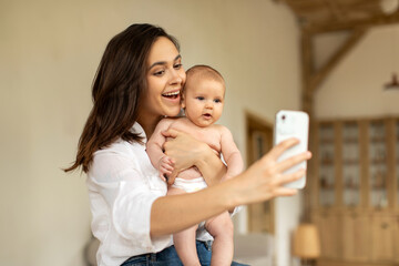 Happy mother making selfie with her cute infant baby daughter, sitting in bedroom at home....