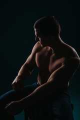 Fit male person sitting on chair and looking aside, posing in studio