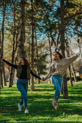 Naklejka na ściany i meble Front view shot of two girls hanging out in the park. They are singing and jumping while walking