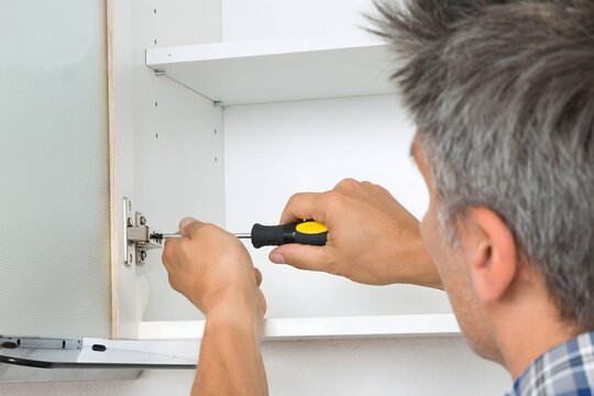 Serviceman Fixing Cabinet With Screwdriver In Kitchen