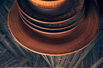 Part of clay plates of different sizes on a dark background. Brown plates are on a wooden shelf. High quality photo