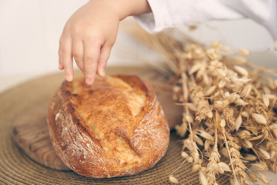 Whole-grain bread lies on the kitchen wooden board, a child's hand touches a loaf. Fresh bread on the table close-up. The concept of healthy food and traditional bakery. High quality photo