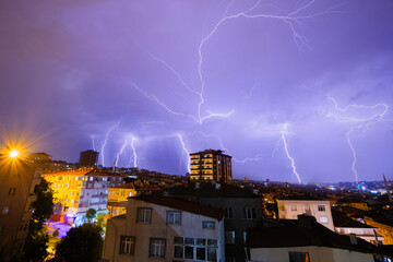 View of stormy sky with rain clouds and bright flashes of lightning strikes during thunderstorm over residential buildings in the city of Istanbul at night