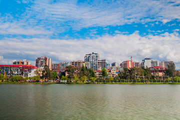 Obraz premium Front view of white clouds over modern apartment buildings. 6 May Park on the shore of lake in Batumi, Georgia in the afternoon. Architecture and nature concept