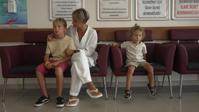 Children and mother are sitting in the hospital corridor, wearing casual clothes and wait the time before their appointment