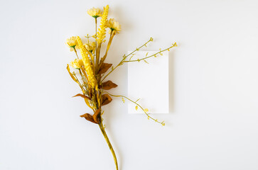 Blank invitation card mockup with a bouquet of yellow flowers on a white background. , top view and flat lay, mockup.