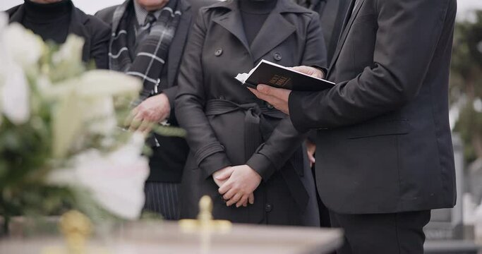 Bible, hands and family at funeral, cemetery or burial ceremony religion by coffin tomb. Holy book, death and grief of people at graveyard, Christian priest reading spiritual gospel and faith in God