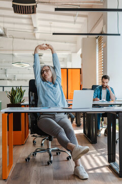 Attractive smiling senior woman stretching arms, relax, taking a break working in modern office. Successful confident businesswoman, entrepreneur finish work