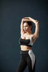 Young fitness woman wearing sportswear standing over dark wall background.