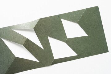 folded and cut green paper shape with triangular cutouts on blank white paper