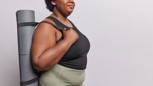 Sideways cropped image of unknown dark skinned obese woman being motivated for training poses with rubber rolled karemat wants to be fitter isolated over white background copy space for your advert