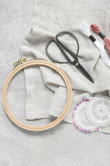 Wooden embroidery hoop with scissors, mouline threads and canvas on grunge grey background