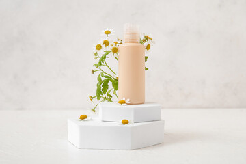 Composition with bottle of cosmetic product, plaster podiums and chamomile flowers on light...