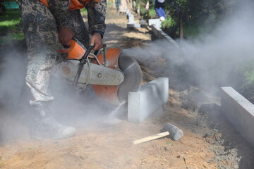 A worker saws a concrete curb with a circular saw, building a pedestrian road.