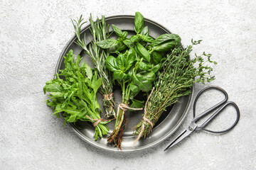 Plate with fresh herbs and scissors on light background