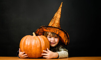 Halloween child in witch hat with pumpkin. Little kid in wizards costume with Halloween...