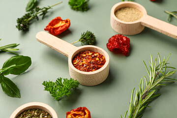 Wooden scoops with spices, dried tomatoes and herbs on color background