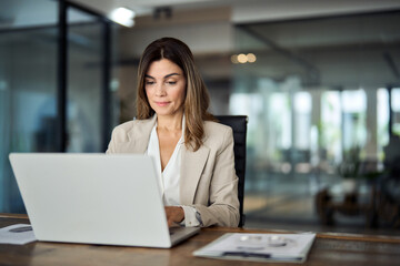 Busy mature middle aged professional business woman manager executive looking at laptop computer technology in office working on digital financial banking market sitting at desk. Copy space. - 639705505