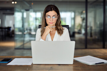 Busy mature middle aged professional business woman manager executive looking at laptop working on...