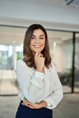 Fototapeta na wymiar Happy cheerful confident Latin professional mid aged business woman in 40s, corporate leader, happy mature female executive, lady manager standing in office looking at camera, vertical portrait.