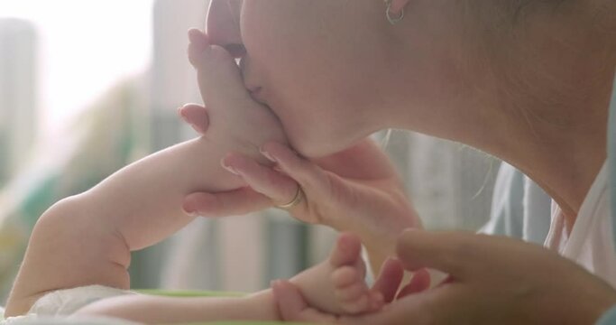mother kisses her newborn baby feet and toes at home, mommy love, happy motherhood.