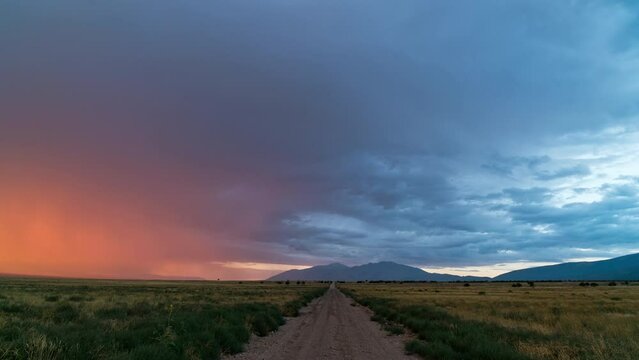 Timelapse looking down dirt road as rain storm is lit by the sun as it fades away.